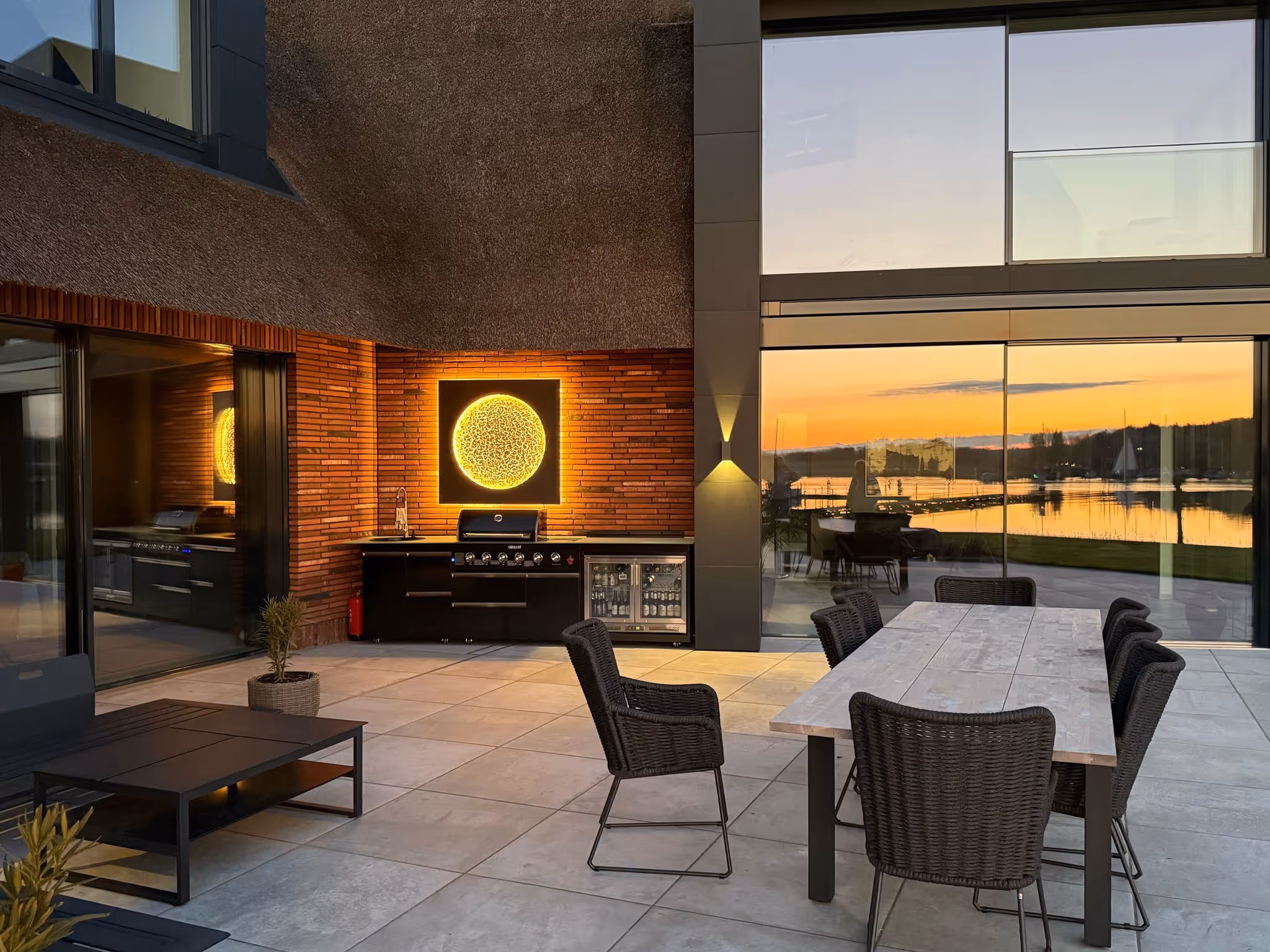 Beleuchteter Sonnenmond aus dem Atelier Kathrin Geller an einer Klinkerwand, Terrasse am See bei Sonnenuntergang