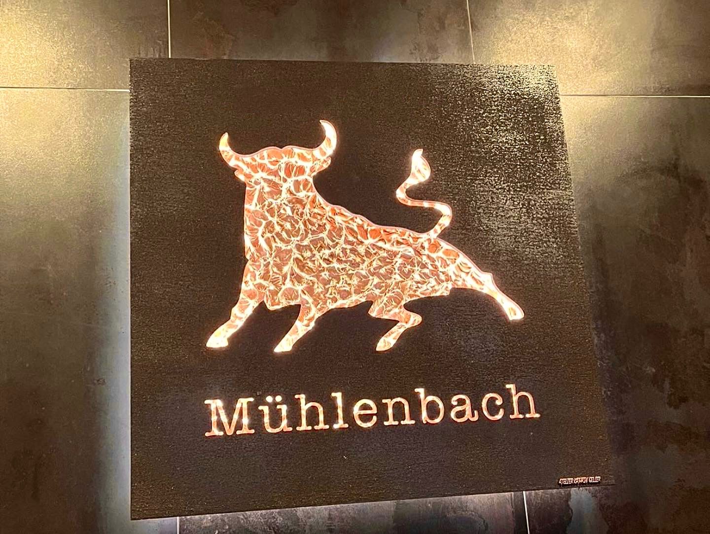 Beleuchteter goldener Stier mit Schriftzug auf dunklem Grund