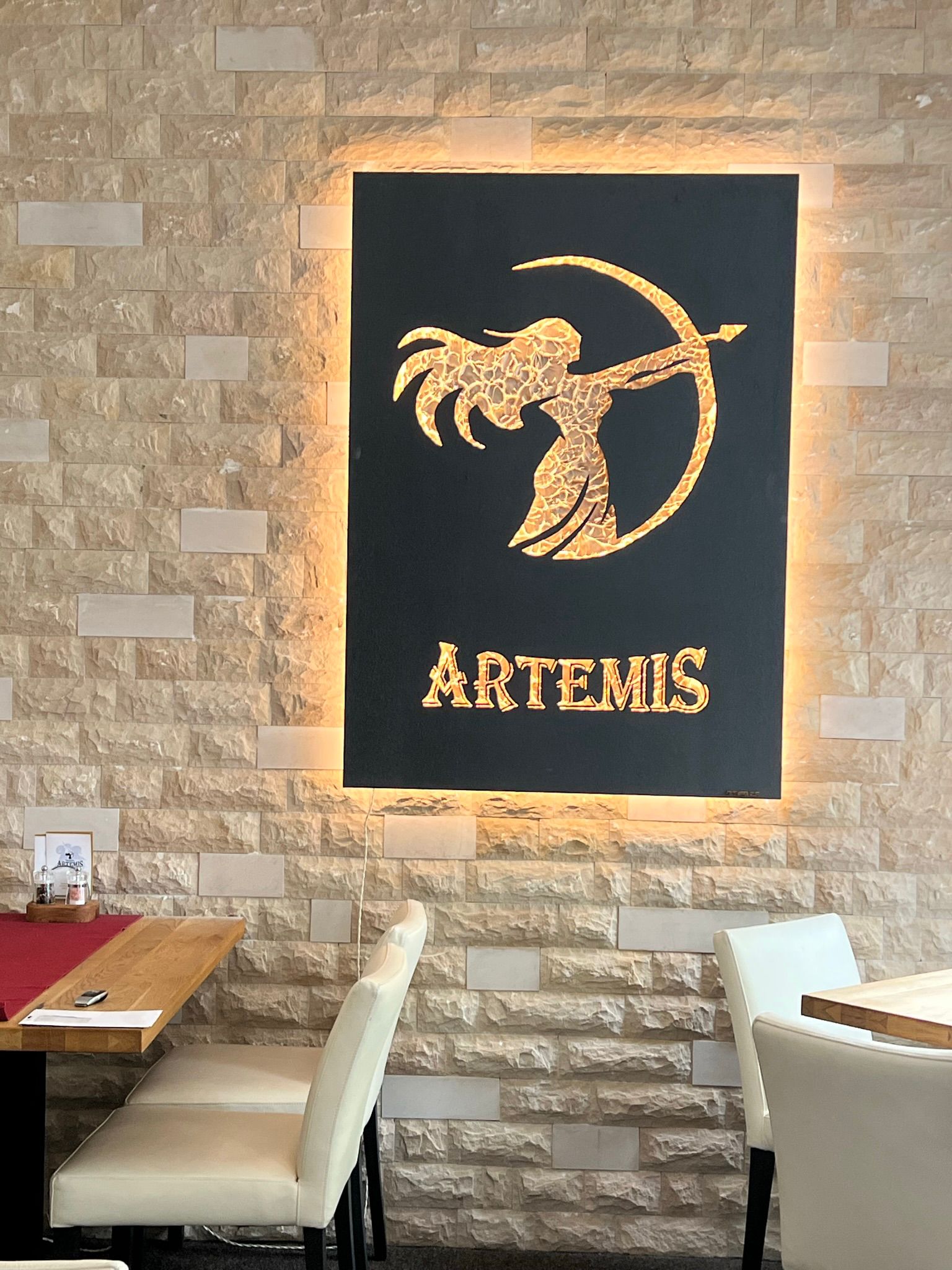Beleuchtetes Logokunstwerk mit Bogenschützin an einer Natursteinwand in einem Restaurant