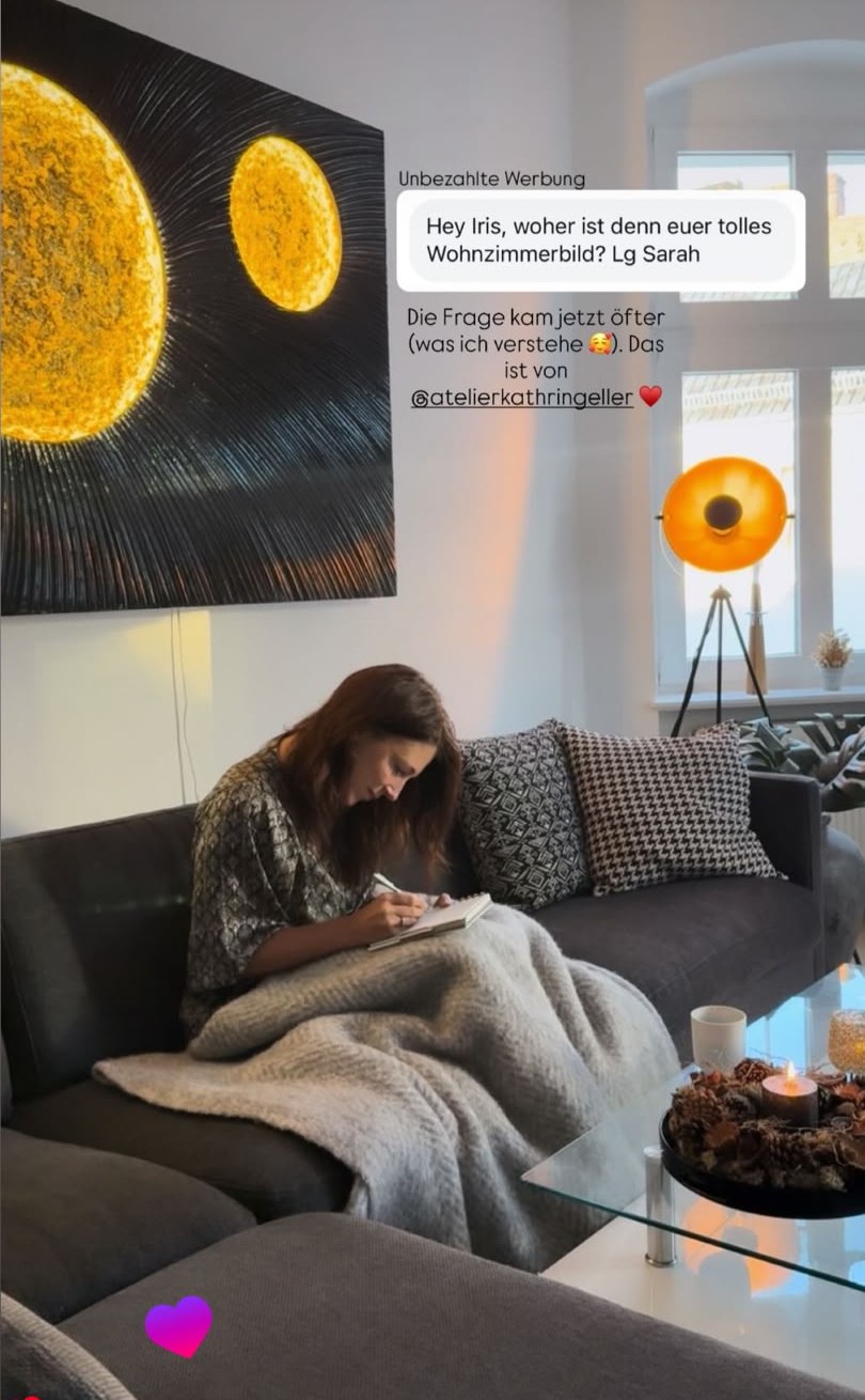 Iris Mareike Steen auf dem Sofa, über ihr ein Lichtkunstwerk mit zwei goldenen Planeten