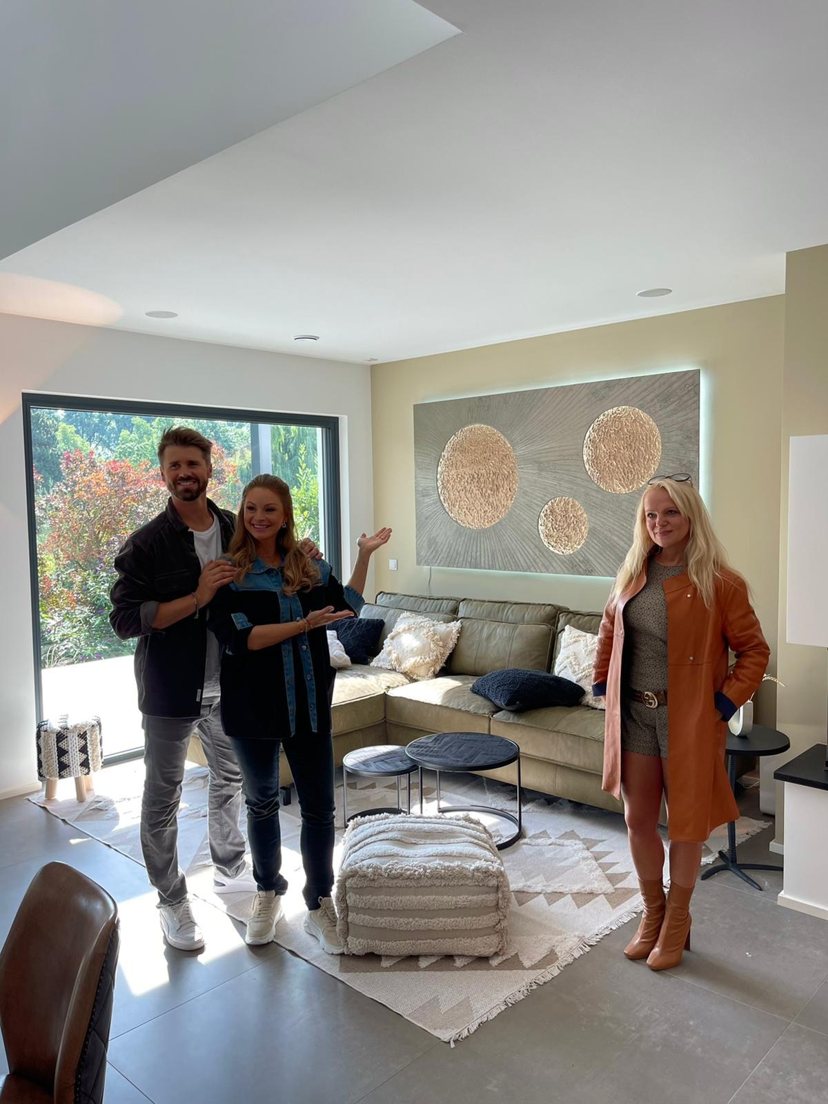 Jana und Thore Schölermann mit Kathrin Geller im Wohnzimmer, an der Wand ein Lichtkunstwerk mit Monden