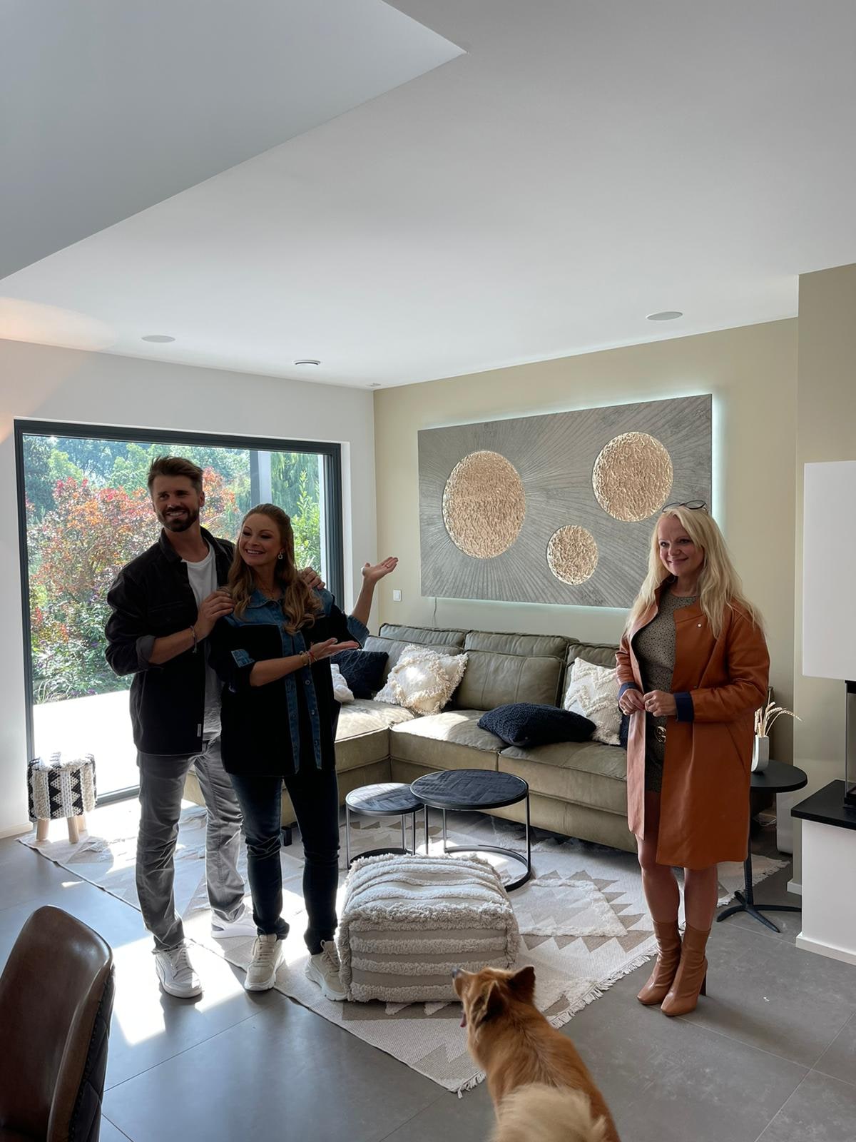 Jana und Thore Schölermann mit Kathrin Geller im Wohnzimmer, Jana zeigt auf das Lichtkunstwerk mit drei Monden